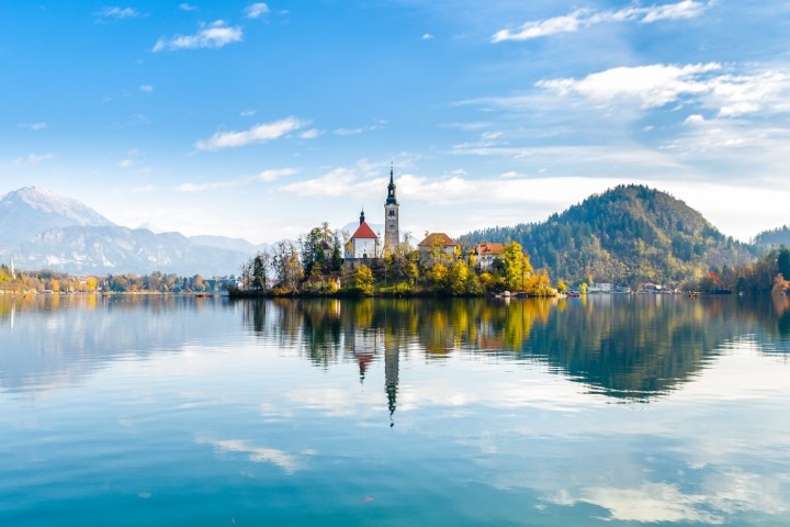 Church on island in a calm lake with mountains and blue sky in the background.