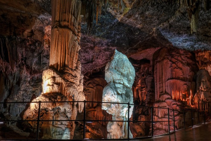 Illuminated stalactites and stalagmites in a vivid underground cave setting.