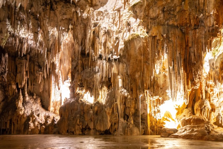 Illuminated cave interior with stalactites and stalagmites.