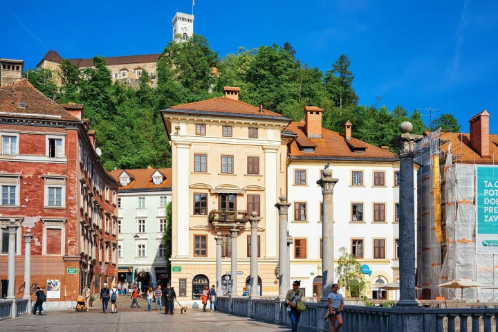 Old town buildings and castle on a hill under blue sky with people walking in the street.