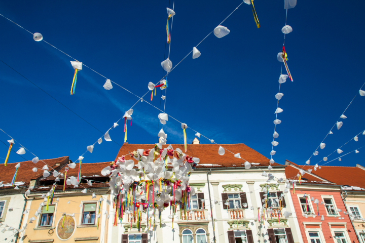 Colorful street decorations with flags and streamers over buildings against a clear blue sky.