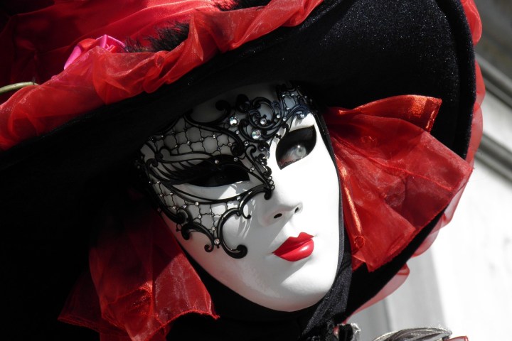 Person in ornate mask and hat with red and black feathers and fabric.