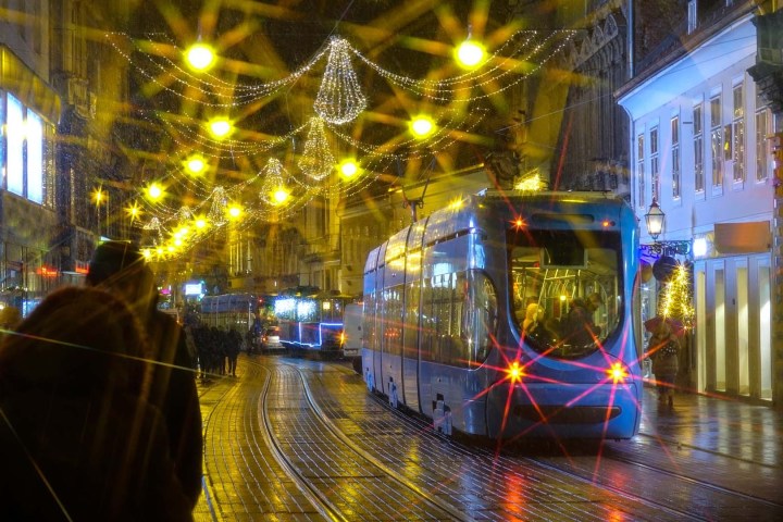 Tram on wet, festive street with bright lights and decorations at night.