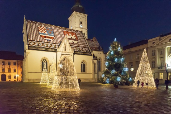 Illuminated Christmas tree and lit decorations in front of a historic church at night.
