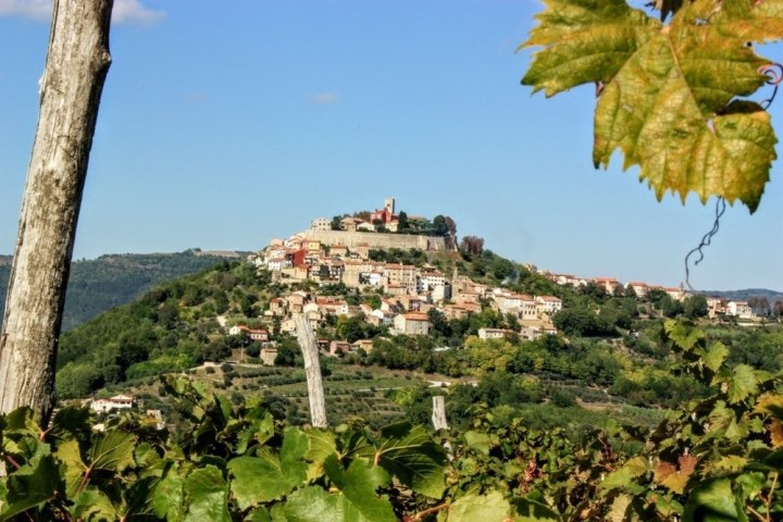 Hilltop village with clustered buildings, surrounded by green foliage and a clear blue sky.