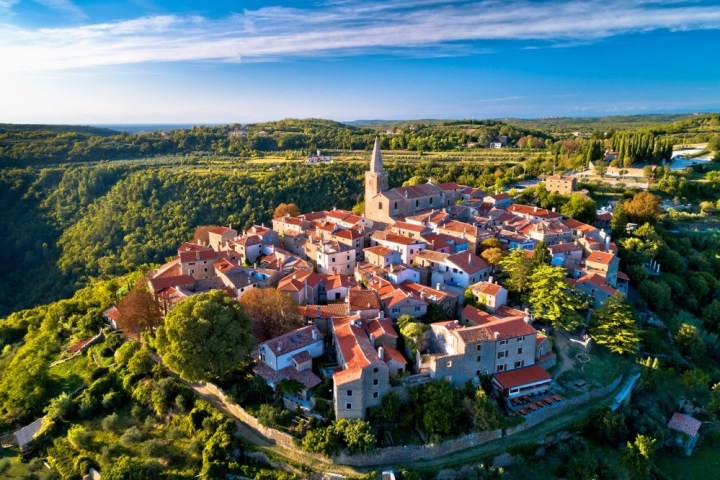 Aerial view of a quaint village with red-roofed buildings surrounded by lush green landscape and a central church tower.