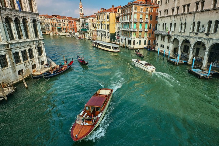 Boats navigate a canal flanked by historic buildings in Venice under clear skies.