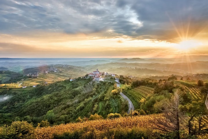Sunset over hilly landscape with a small village and winding roads.