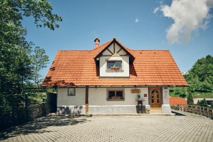 A quaint house with a red-tiled roof and flowers under windows, surrounded by greenery and blue sky.