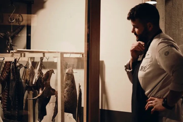 Chef examining hanging cured meats in a display case.