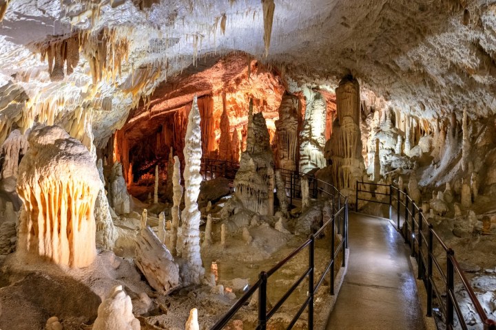 Illuminated cave with stalactites, stalagmites, and a pathway with railings.