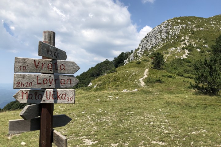 Wooden signpost on grassy hill with mountain and cloudy sky background.