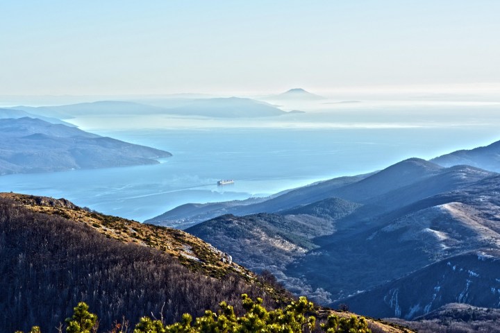 Coastal mountain range with a large ship sailing on the ocean in the background.
