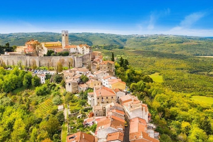 Aerial view of a hilltop town with a castle and surrounding countryside under a clear blue sky.