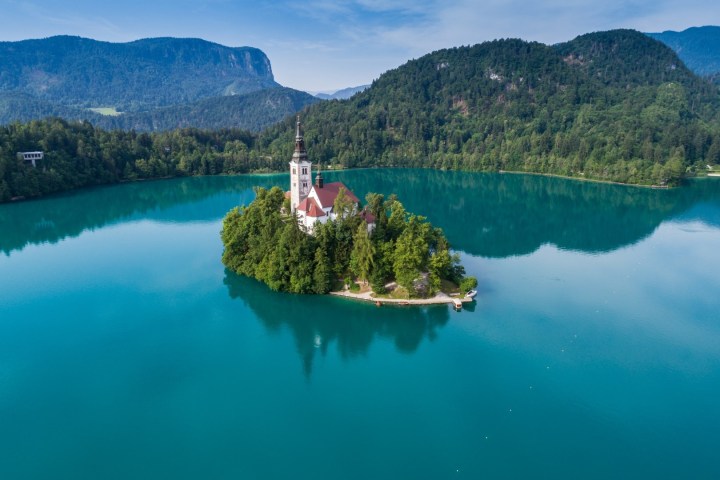 Island with church on turquoise lake surrounded by forested hills and mountains.