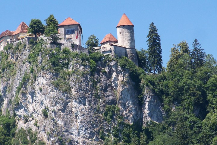 Castle with orange roofs on a cliff surrounded by trees and a clear blue sky.
