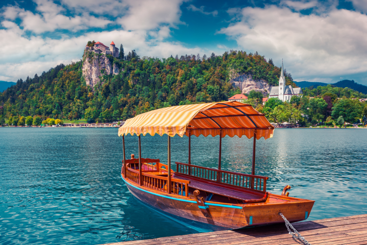 Wooden boat with canopy on lake, castle on hill, church in background.
