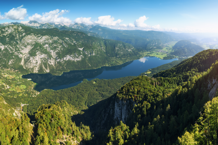 Panoramic view of a mountainous landscape with a lake and lush green forests under a clear blue sky.