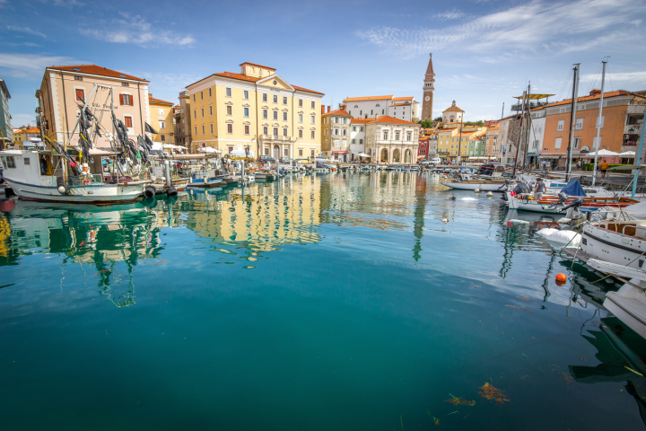 Scenic waterfront with boats and colorful buildings reflected in calm water.