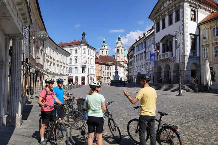 Group of cyclists in a European square with historic buildings under a clear blue sky.