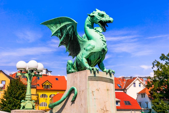 Green dragon statue on a pedestal with red-roofed buildings in the background.