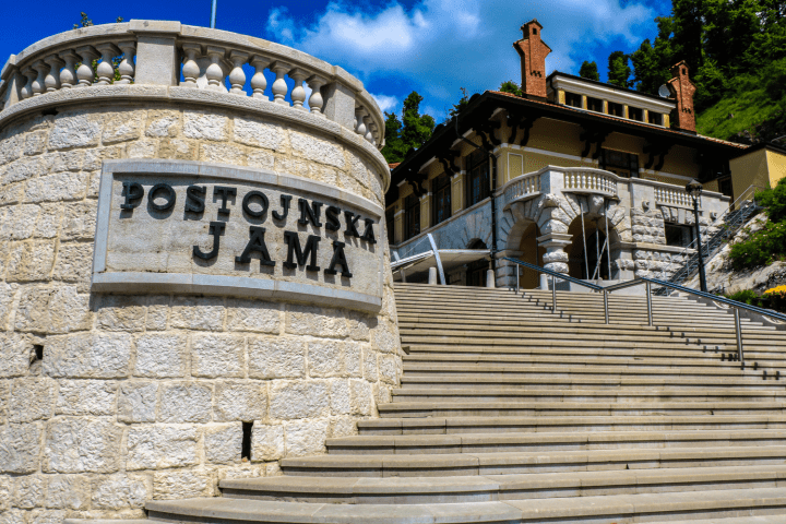 Stone steps leading to a historic building with 'Postojnska Jama' sign.