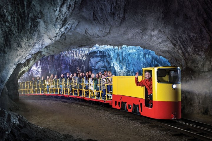 Yellow train with passengers inside a large cave with rocky walls.