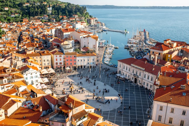 Aerial view of a coastal town square with colorful buildings and a marina by the sea.