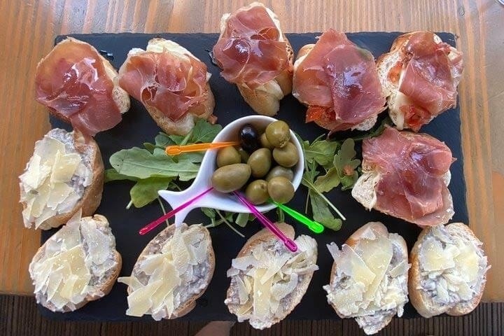 Appetizers with ham, cheese, and a bowl of olives on a slate platter.
