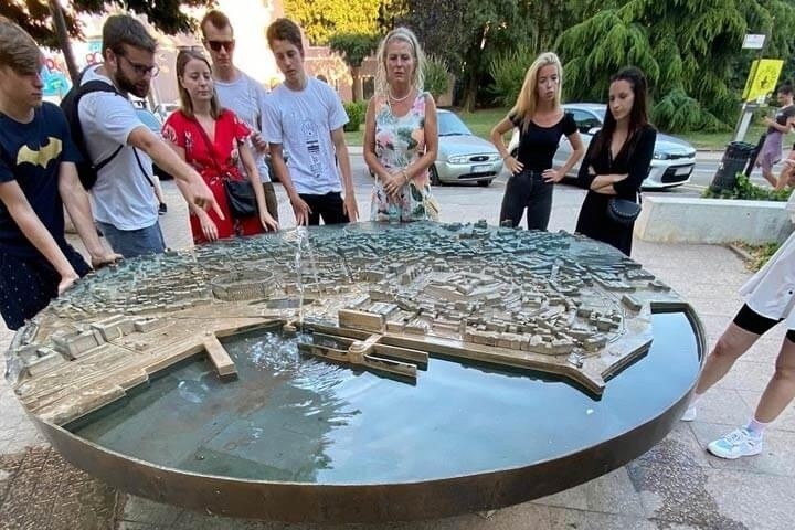 People gathered around a circular 3D model of a cityscape on display outdoors.