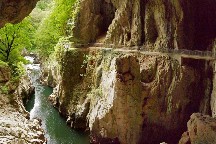 River flowing through rocky gorge with scenic walkway along cliff edge.