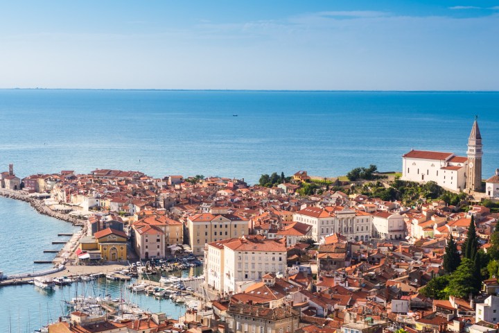 Aerial view of a coastal town with red-roofed buildings and a church by the sea under a clear blue sky.