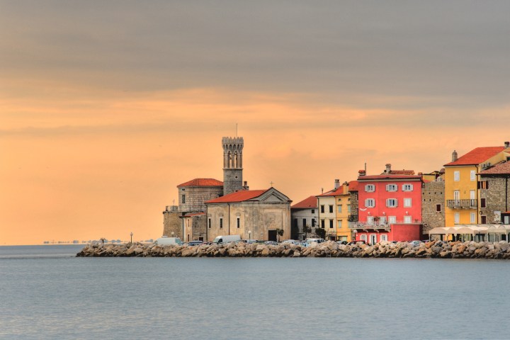 Coastal town with colorful buildings and a church under a warm sunset sky.