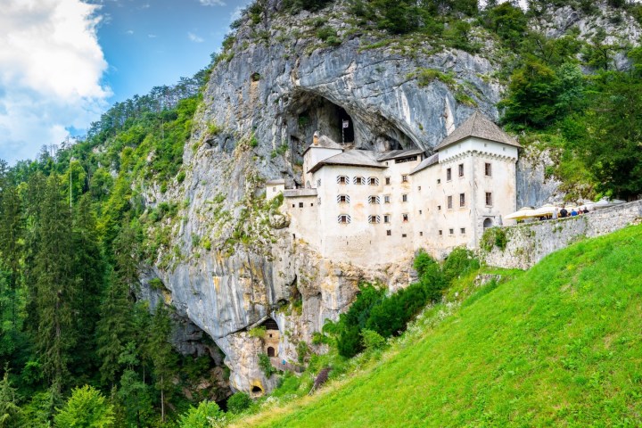 Castle built into a rocky cliff with greenery and blue sky in the background.