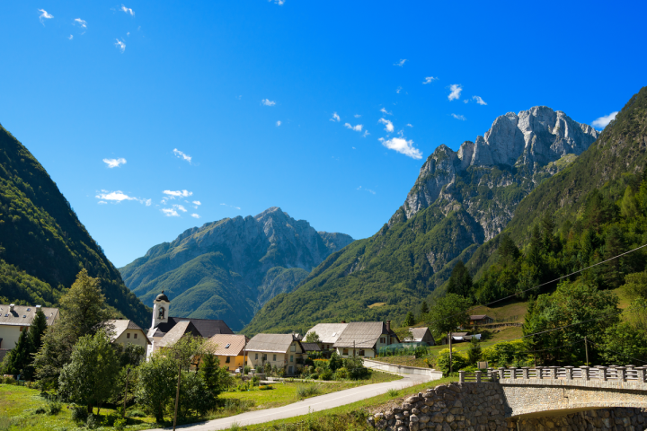 Village with a church and houses in a valley surrounded by mountains under a clear blue sky.
