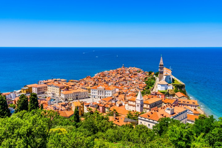 Coastal town with red roofs and a prominent church by the sea under a clear blue sky.