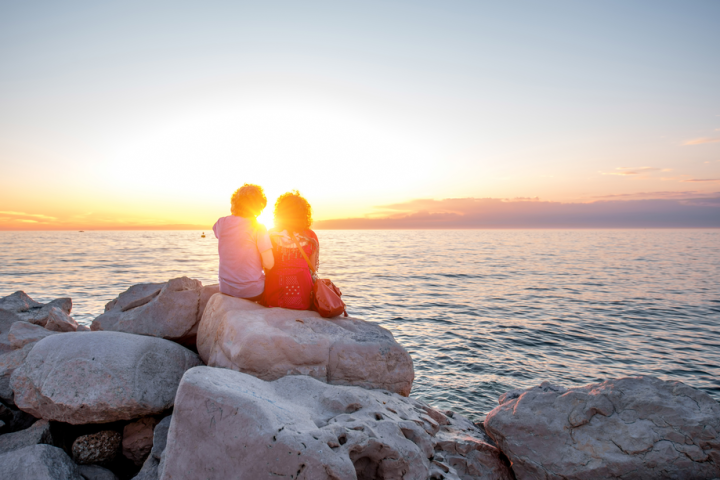 Two people sitting on rocks by the sea, watching a sunset.
