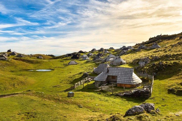 Rustic wooden cabins in a lush green valley under a blue sky.