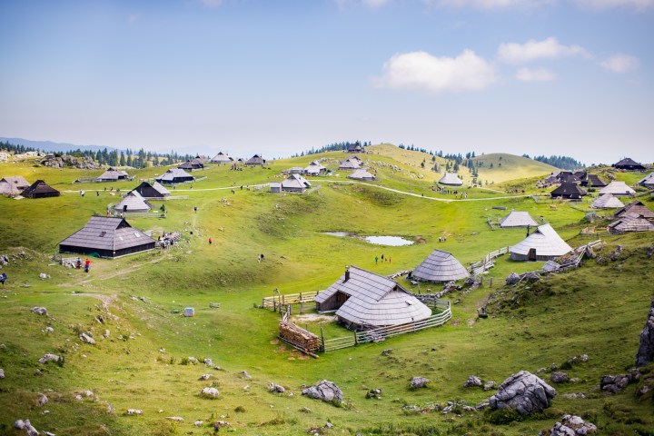 Traditional huts scattered across a lush green landscape with rolling hills and a few small ponds.