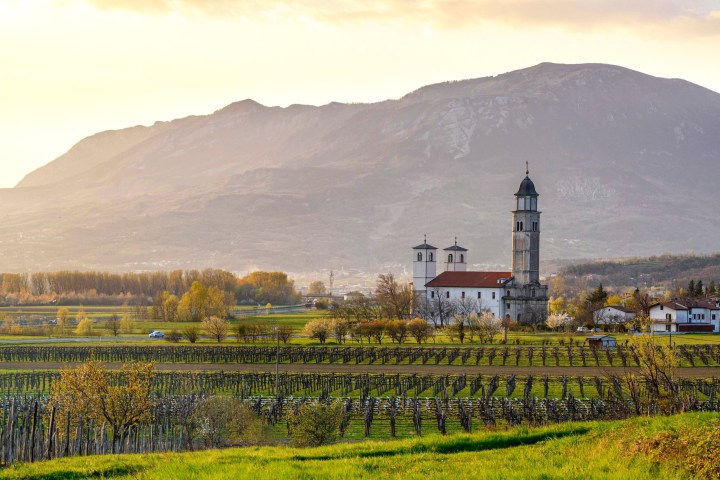Church with two towers in a rural landscape with vineyards and mountains at sunset.