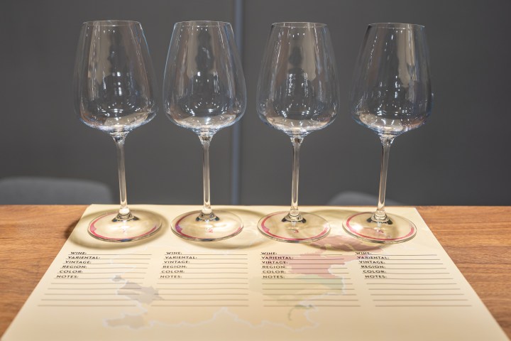 Four empty wine glasses on a tasting notes sheet on a wooden table.
