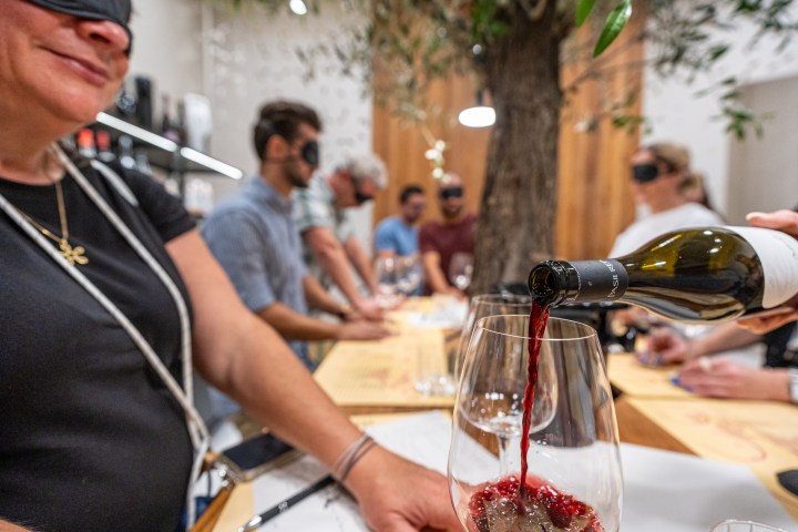 People blindfolded during wine tasting, red wine poured into a glass.
