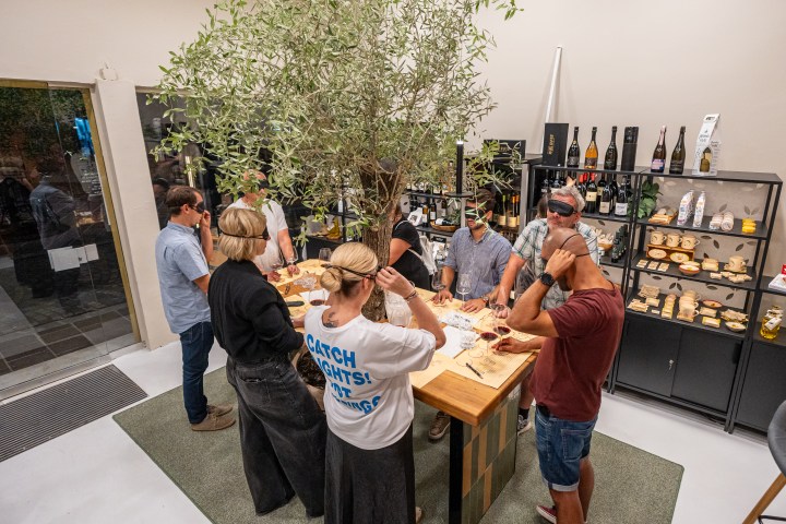 Group of blindfolded people at a tasting event around a table with wine and snacks.