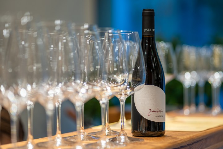 A wine bottle beside multiple empty wine glasses on a wooden table.