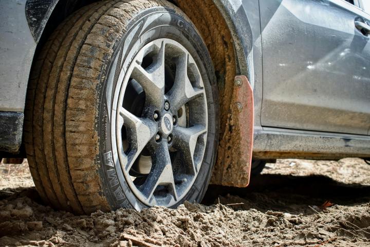 Car tire partially buried in mud, showing alloy wheel and mud flap.